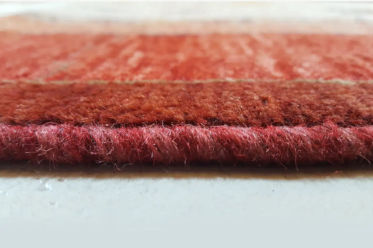 Close-up of the carpet edge: dense pile, reddish-brown woven texture with a white backing