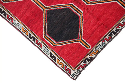 Corner view: red Lori rug with a black hexagon pattern and decorative trim