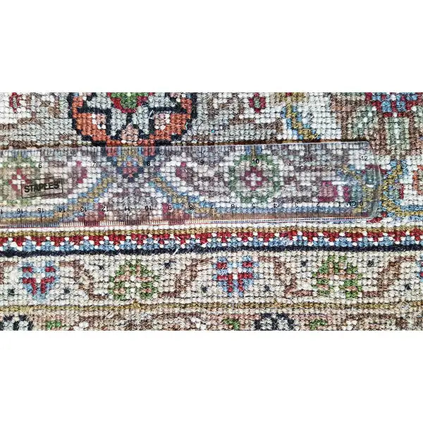 Rug: Close-up of a patterned border with colorful ornamental inlays and a light background.