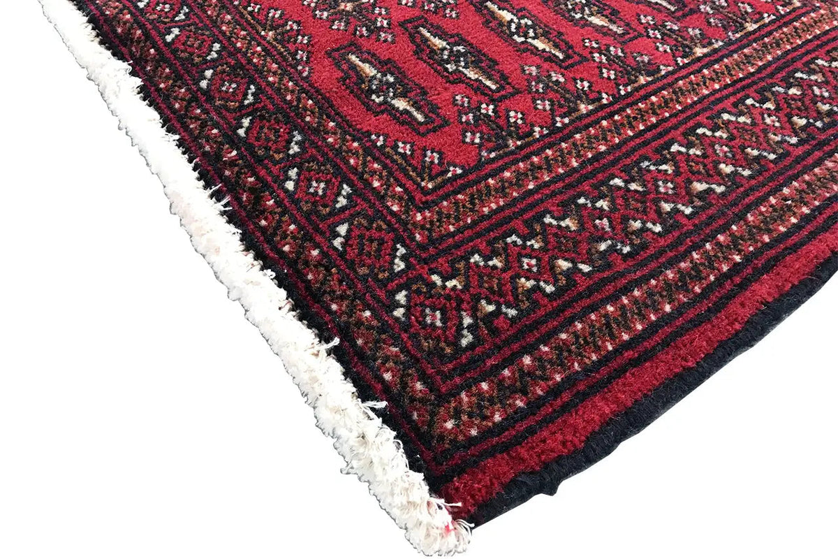 Turkmen carpet corner with a dark red pattern, borders, and light-colored fringes along the edge