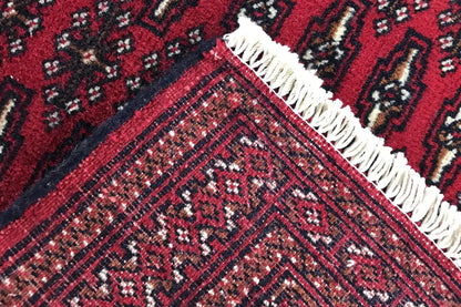 Close-up: Turkmen carpet with a dark red ornamental pattern and fringes along the edge