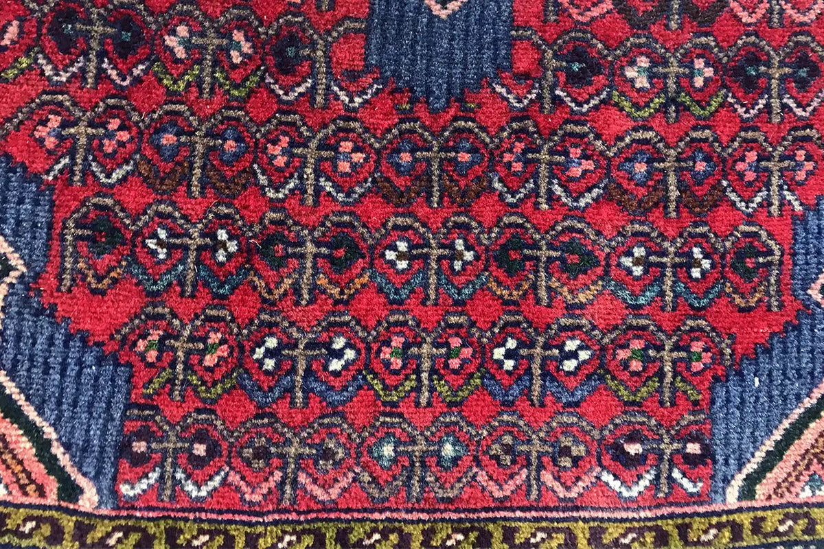 Detail of an oriental rug with a red and dark blue vine and diamond pattern