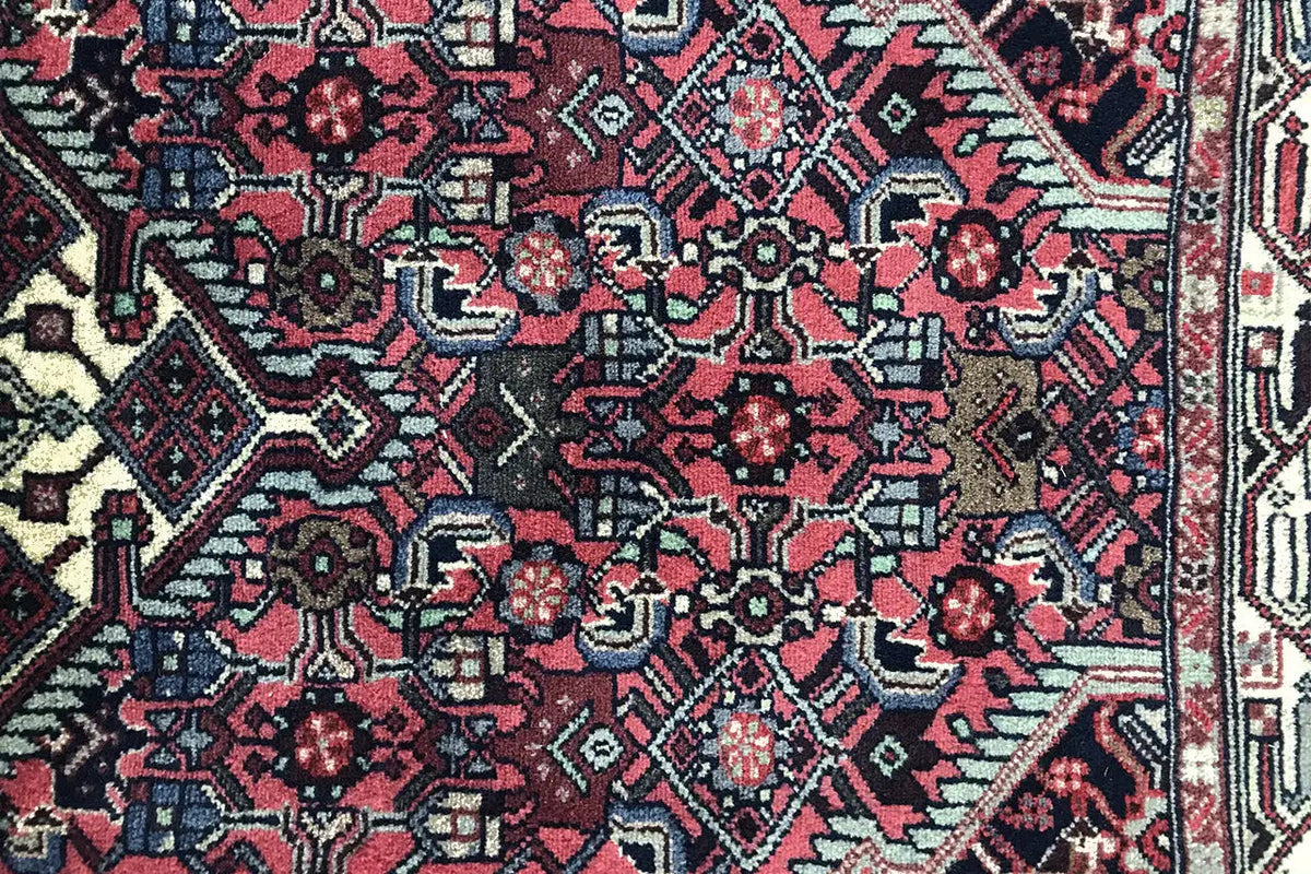 Detail view of Hamadan rug: red field with dark blue motifs and a geometric border band