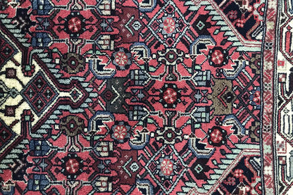 Detail view of Hamadan rug: red field with dark blue motifs and a geometric border band