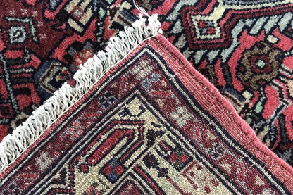 Close-up of a corner of a Hamadan rug with fringes and a red border, cream-colored patterned lines