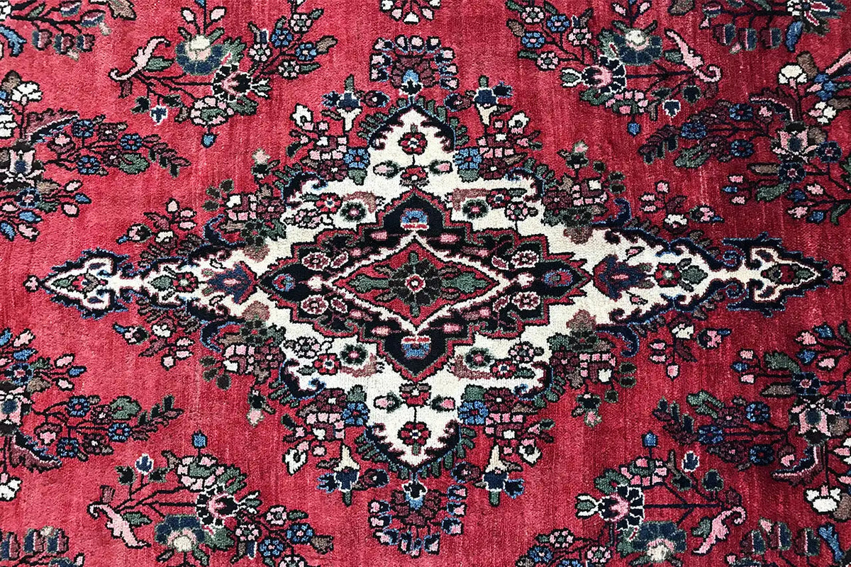 Close-up of a Hamadan rug: red background with floral vines and a central pattern