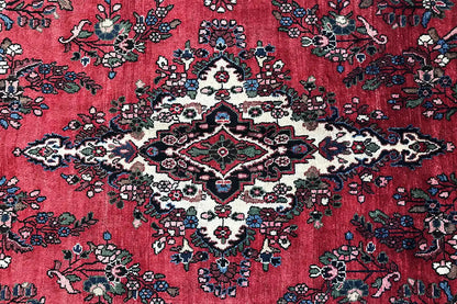 Close-up of a Hamadan rug: red background with floral vines and a central pattern