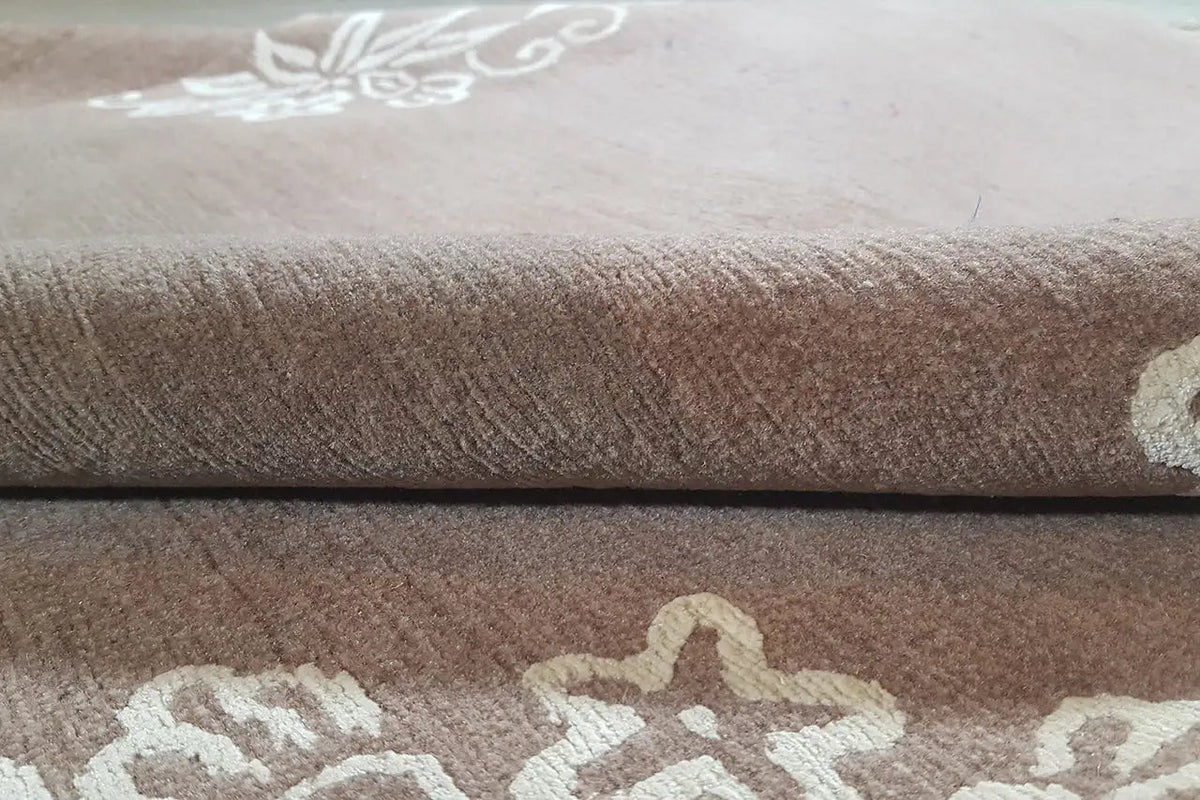 Designer rug with brown pile and cream-colored ornamental pattern, folded
