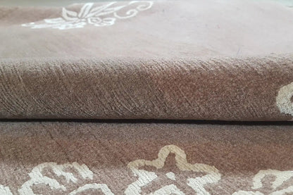 Designer rug with brown pile and cream-colored ornamental pattern, folded