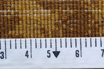 Close-up of a carpet: brown woven material with white fringe along the edge