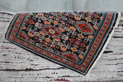 Rectangular Oriental rug with a dark blue pattern, red border, and fringes