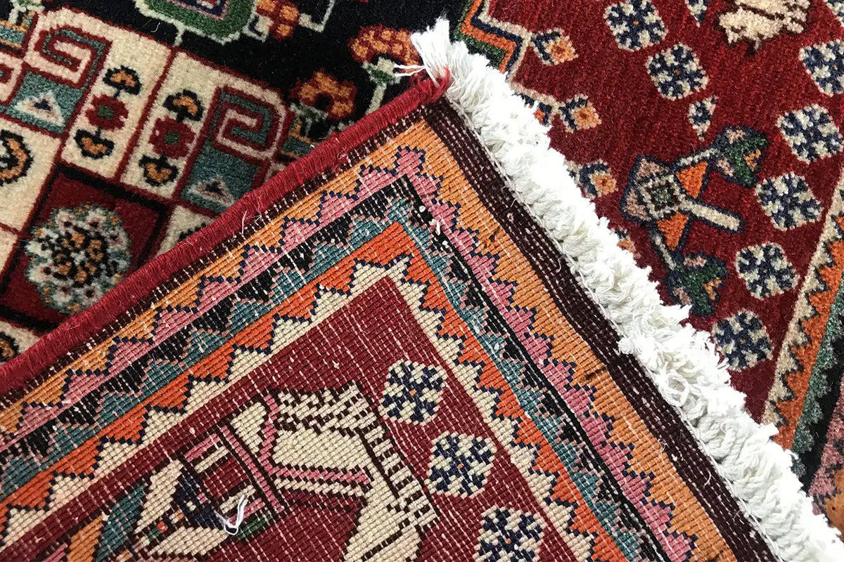 Detail at the edge: fringed selvedge, burgundy border, black field, and colorful ornamentation