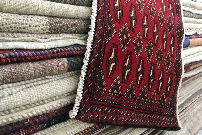 Poshti Turkmen carpet (95x47 cm) on folded textiles, red with a dark border