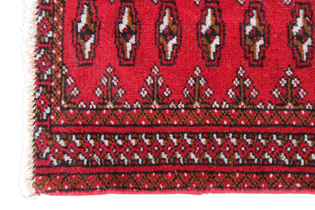 Turkmen carpet close-up: red runner with rows of ornaments and white fringed edges