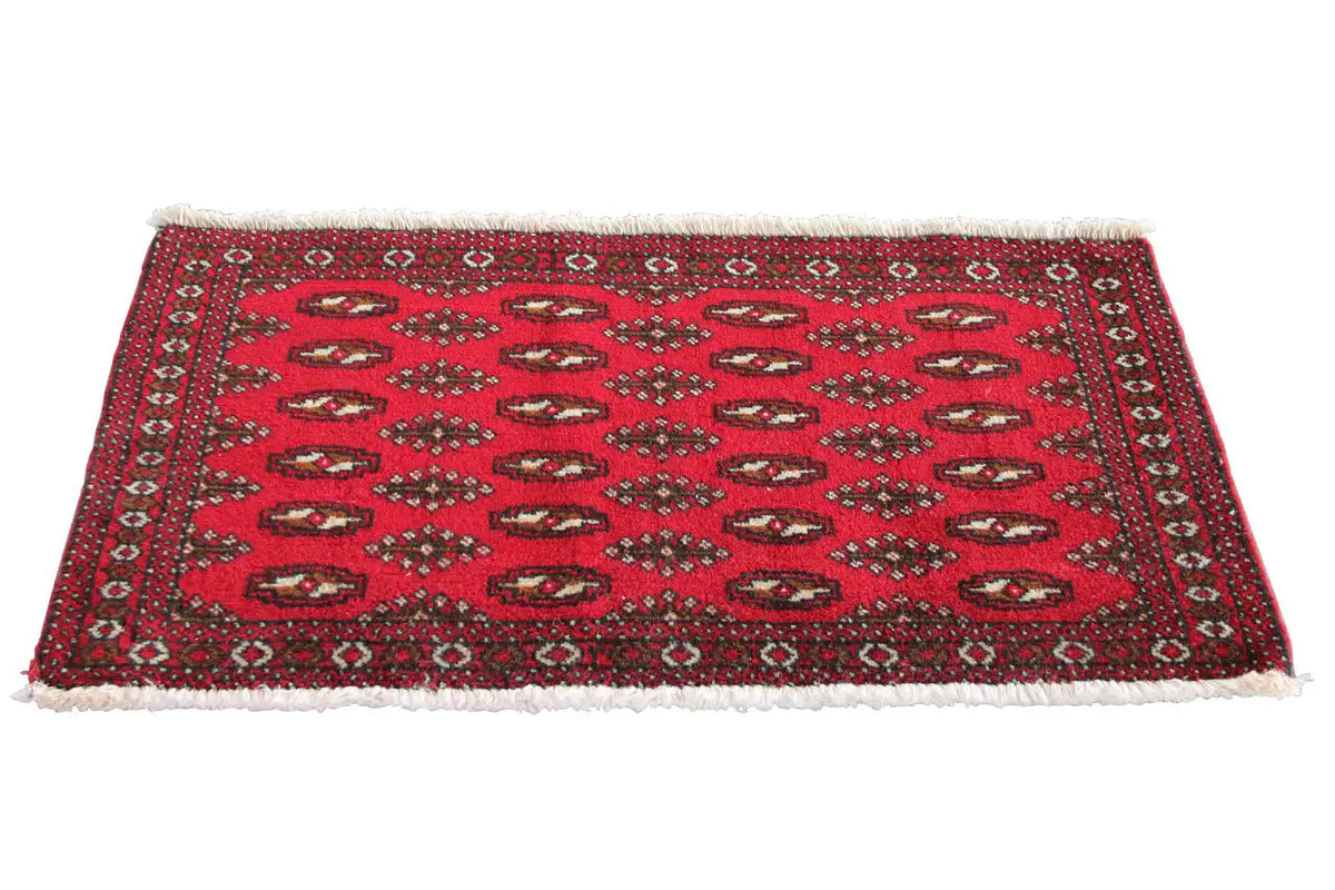 Red patterned Turkmen carpet with small medallions, dark border and fringes