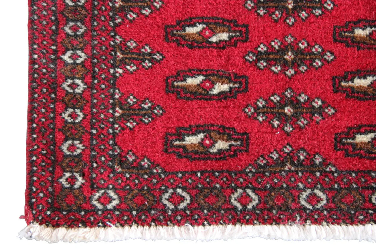 Close-up: red Turkmen carpet with an ornamental border and white fringes at the bottom