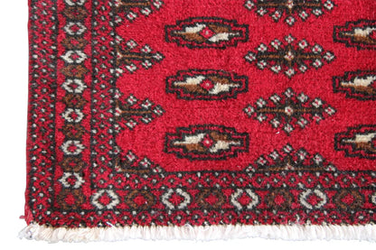 Close-up: red Turkmen carpet with an ornamental border and white fringes at the bottom