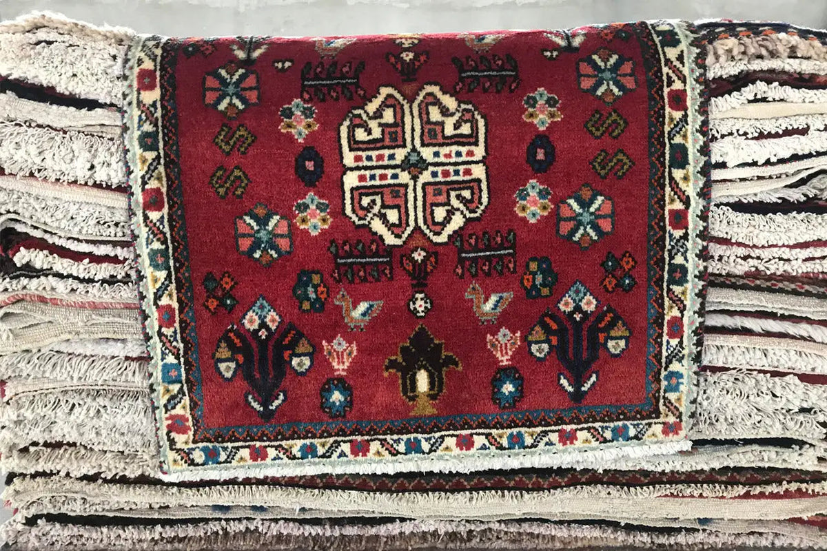 Red Oriental rug with a colorful medallion and fringes, on stacked layers of rugs