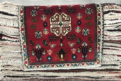 Red Oriental rug with a colorful medallion and fringes, on stacked layers of rugs