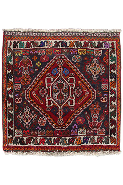 Rug in a 59x59-cm format with an oriental pattern in red, blue, and dark gray, with fringes.