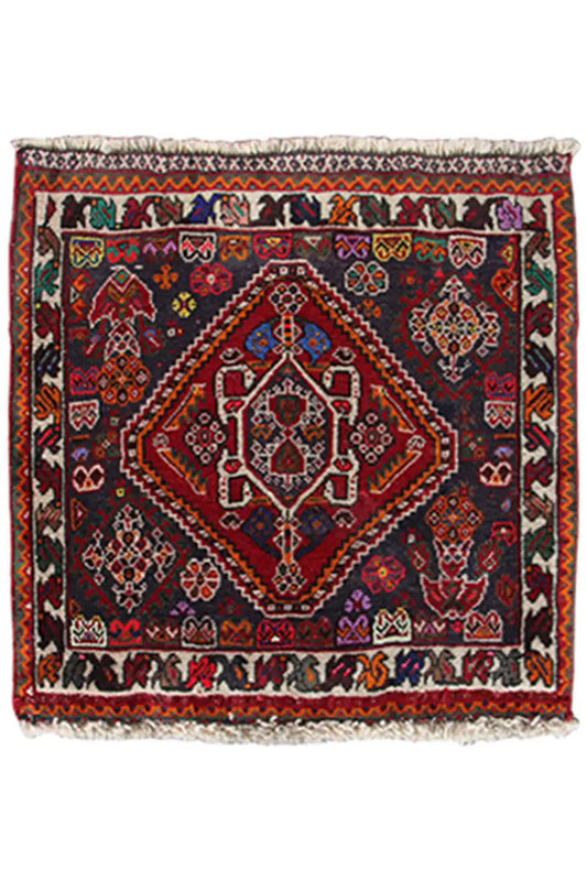Rug in a 59x59-cm format with an oriental pattern in red, blue, and dark gray, with fringes.
