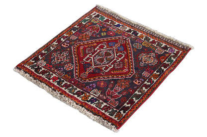 Rug with a red central field and dark border pattern, square-shaped with light-colored fringes.