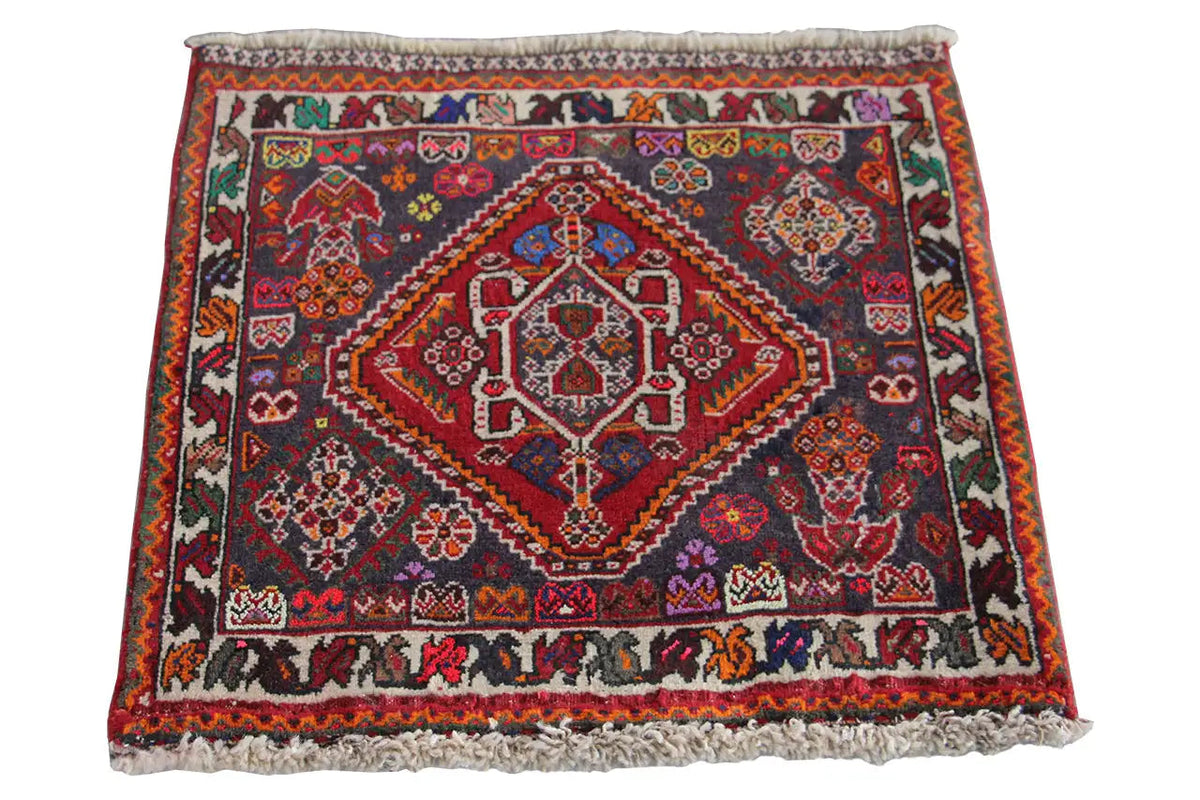 Square rug 59x59 cm with a red central motif and colorful decorations, with fringes all around.