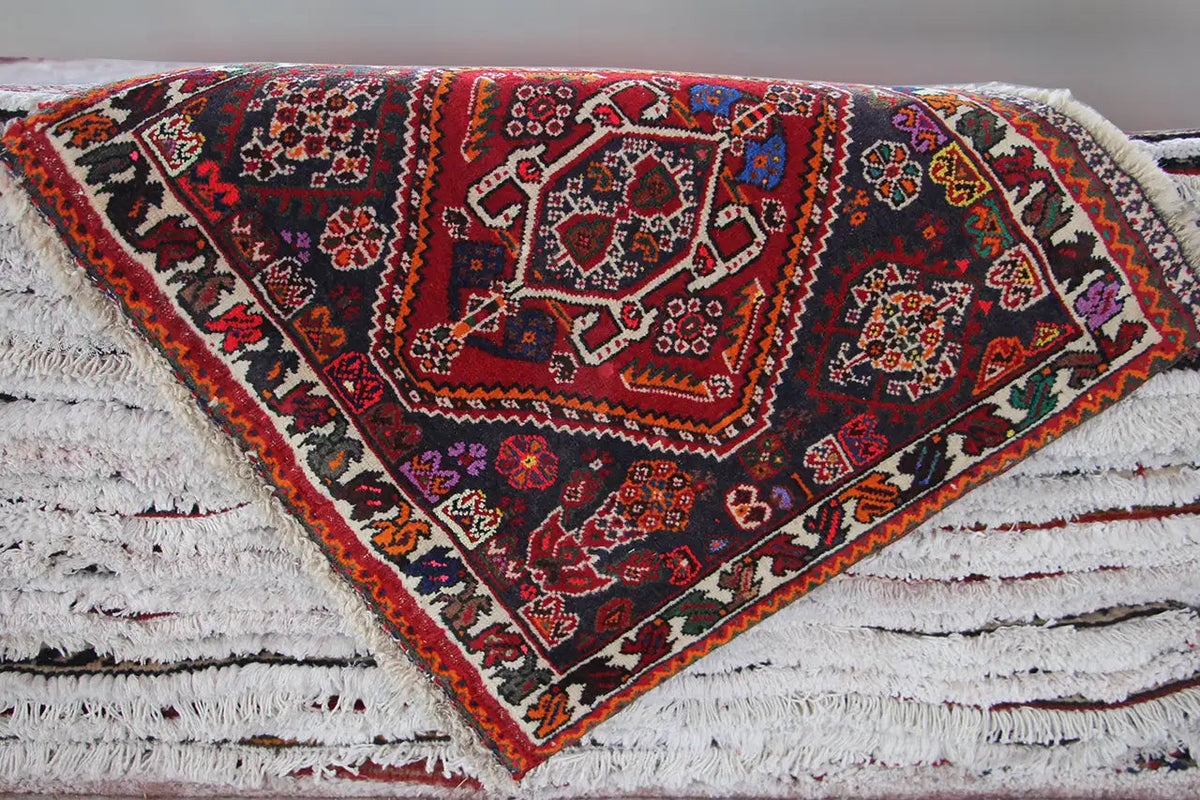 Rug on a white background: central red medallion, dark ornaments, and fringed edges.