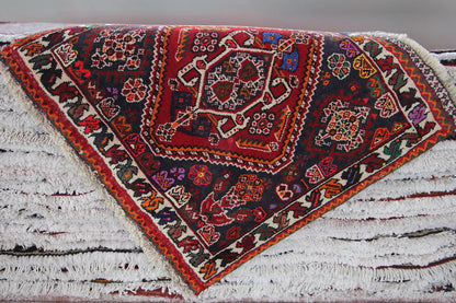Rug on a white background: central red medallion, dark ornaments, and fringed edges.