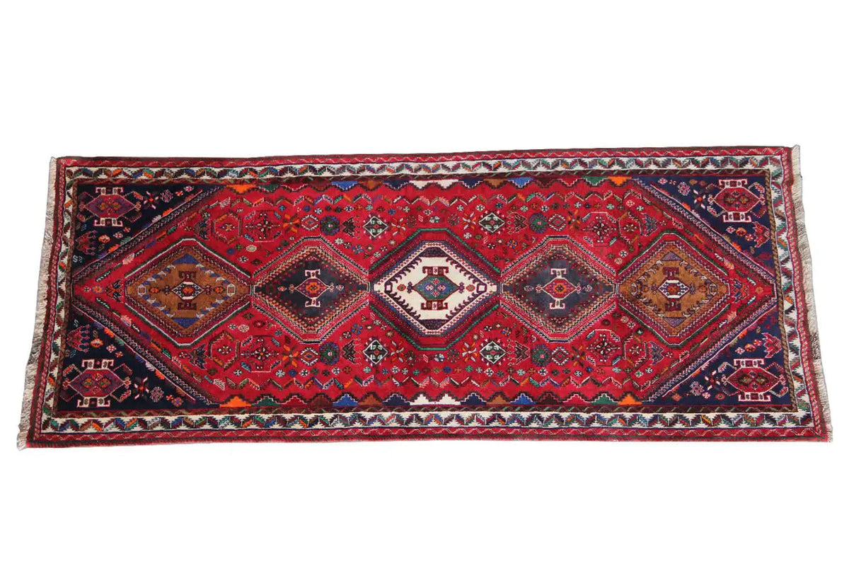 Oriental rug runner with red, blue and green ornaments, a wide border, and fringes