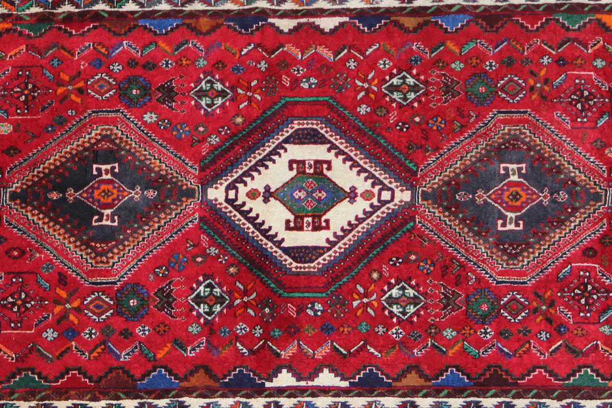 Oriental runner rug with a detailed red pattern, central diamonds, and a blue decorative border