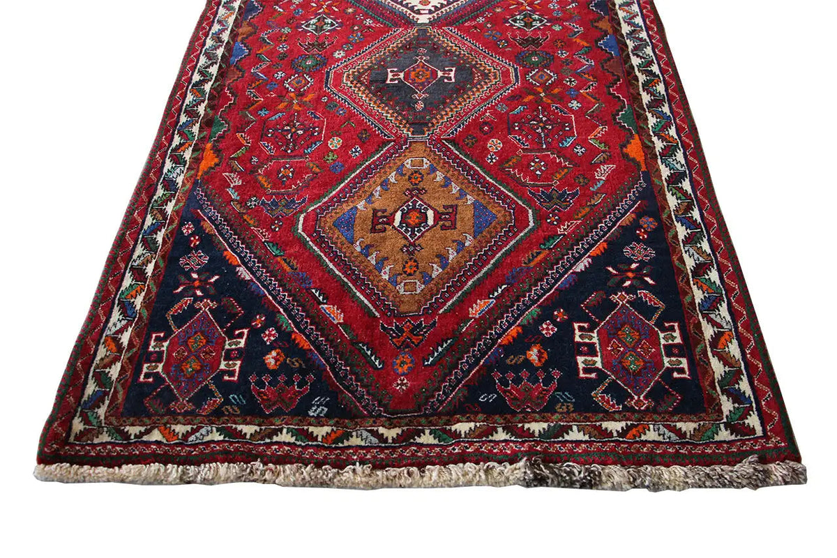 Oriental rug runner close-up: red geometric diamonds, turquoise/green accents, fringes along the edge