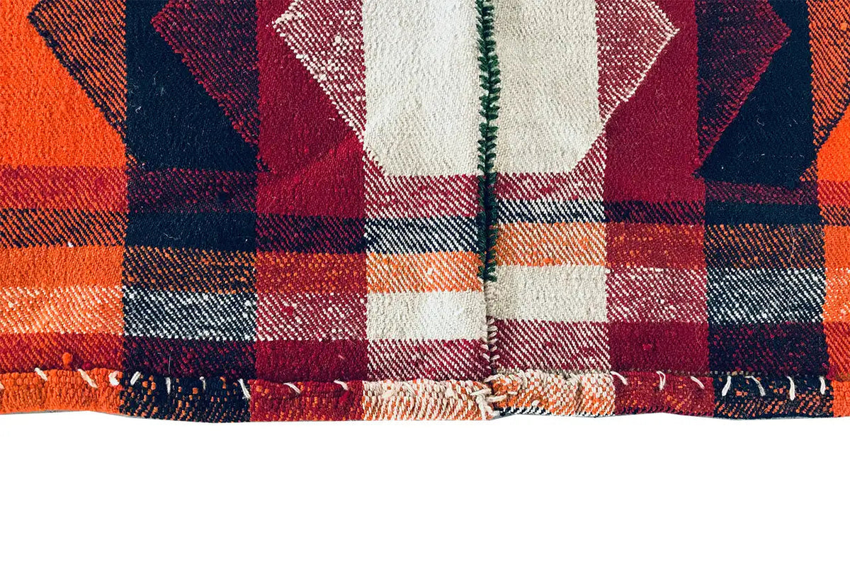 Close-up of a jajim rug: checked fabric in orange, dark blue, and burgundy with fringes