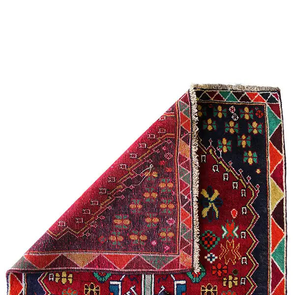 Carpet corner with a red and dark blue pattern, colorful decorative stripes, and fringed trim