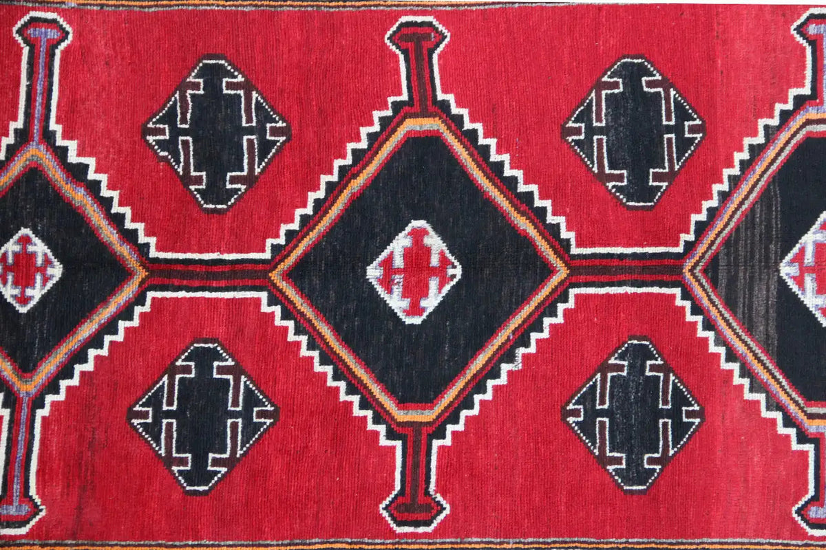Lori rug with a red background, black decorative panels, and geometric diamonds in beige and blue.