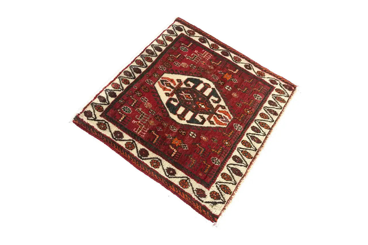Rug viewed at an angle: red patterned field with a white border and fringes