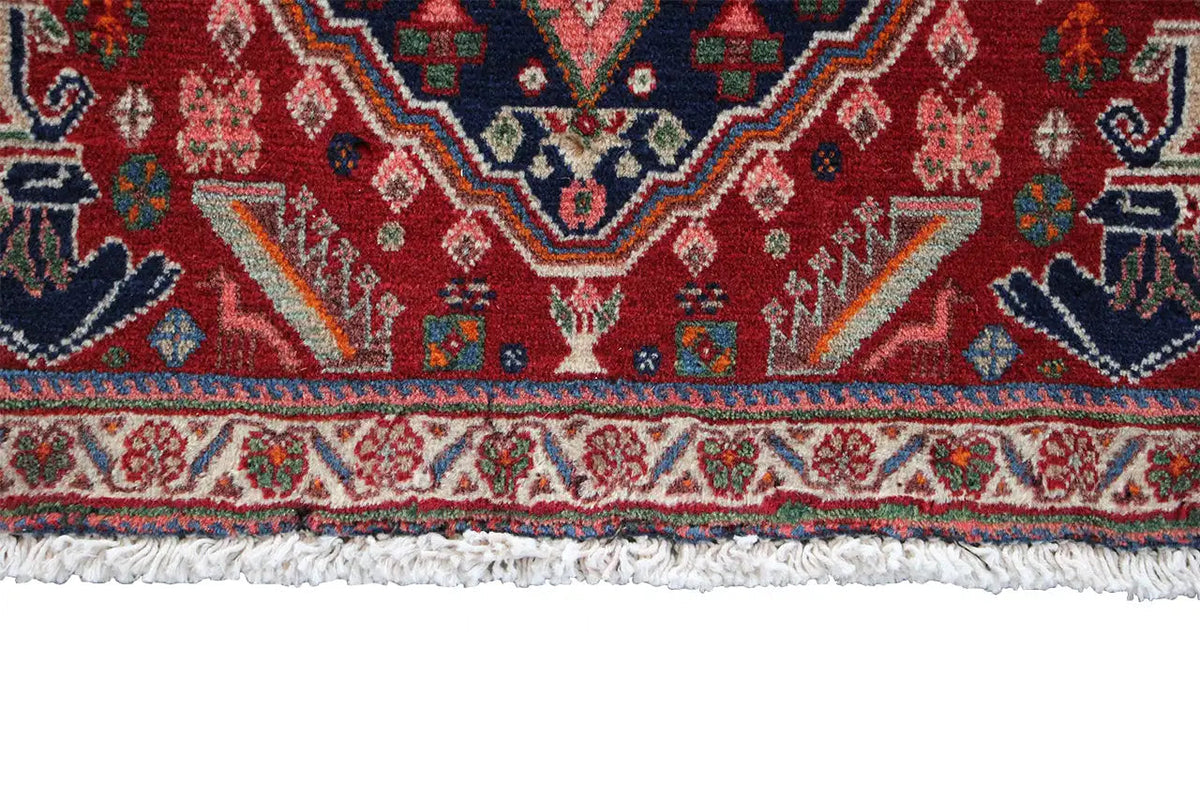 Lower edge of an Oriental rug with fringe and a colorful border pattern on a red background