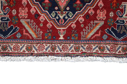 Lower edge of an Oriental rug with fringe and a colorful border pattern on a red background