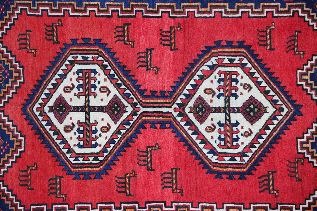 Oriental rug with a red field, blue border, and white decorative diamonds, close-up.