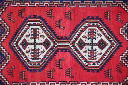 Oriental rug with a red field, blue border, and white decorative diamonds, close-up.