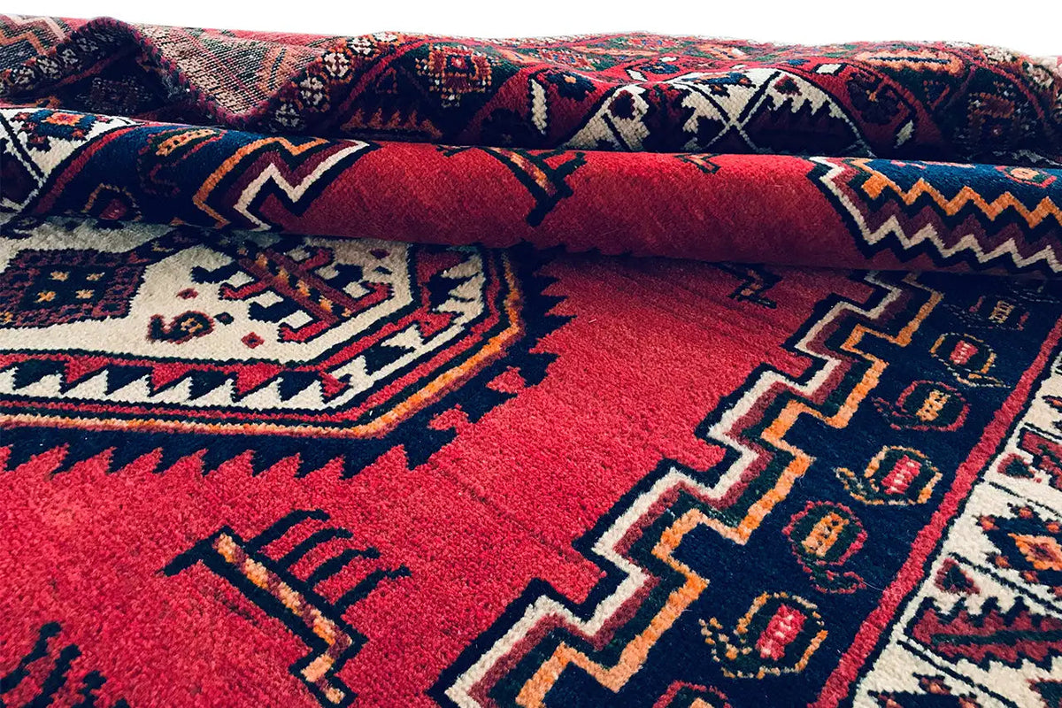 Folded oriental rug with a red background, blue patterns, and white accents.
