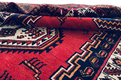 Folded oriental rug with a red background, blue patterns, and white accents.