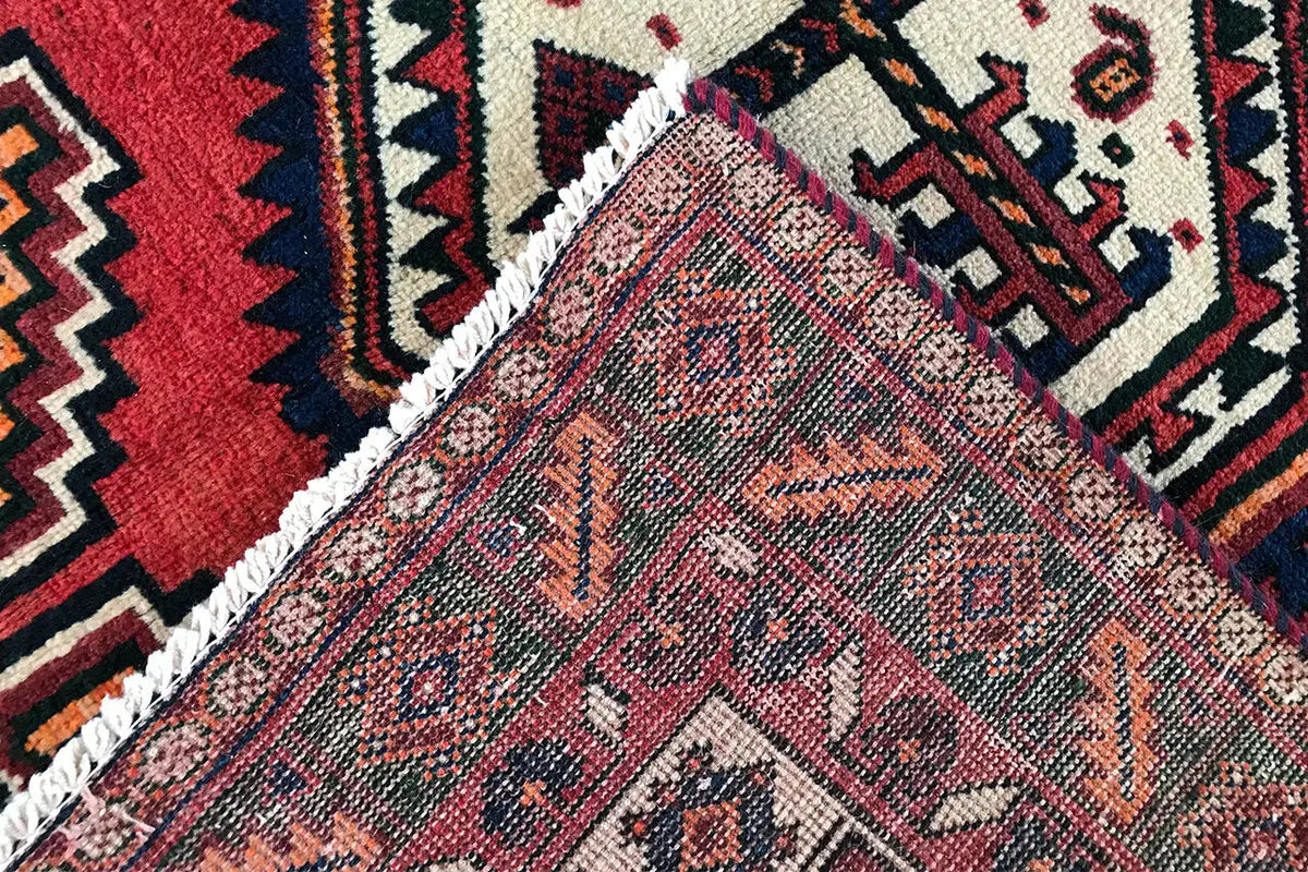 Oriental rug detail with a red background, blue-and-white ornaments, and a braided border.