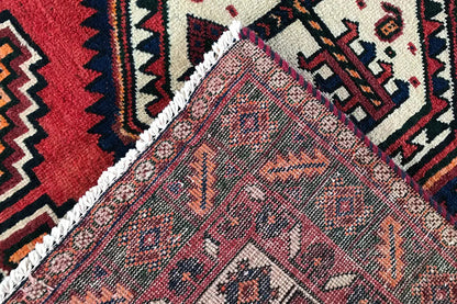 Oriental rug detail with a red background, blue-and-white ornaments, and a braided border.