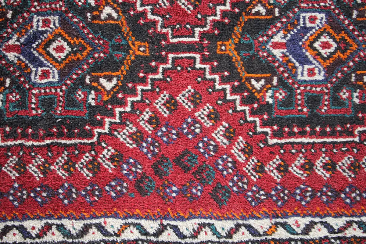 Close-up of a rug: red pattern with blue-gray medallions and zigzag decorative lines
