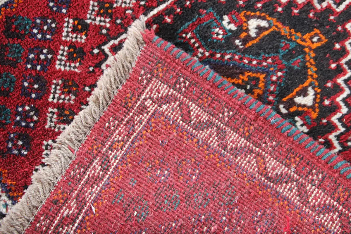Corner of a red oriental rug with a dense weave, fringe, and colorful ornaments