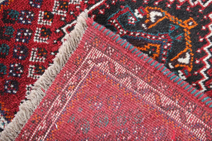 Corner of a red oriental rug with a dense weave, fringe, and colorful ornaments