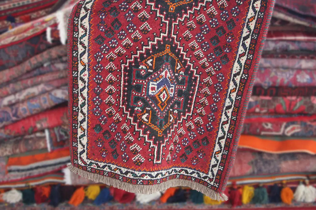 Folded Oriental rug with a red pattern and light border stripes, fringes along the edge