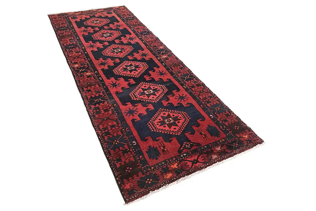 Red runner rug with a blue pattern and geometric medallions, fringed edges.