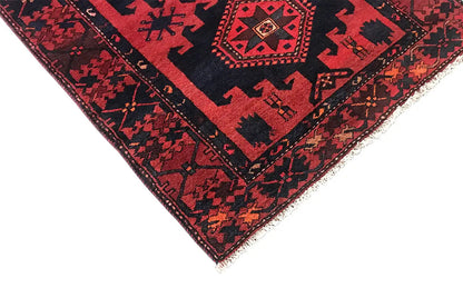 Detail of a red runner rug with blue border trim, fringes, and a geometric pattern.